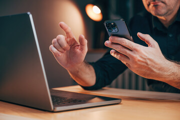 Businessman using laptop computer and smartphone in office while working overtime