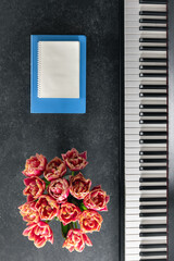 Piano, bouquet of flowers and notepads on a dark background, top view.