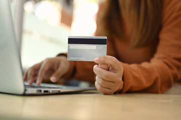 Select focus on woman hand holding a credit card and using laptop on wooden table