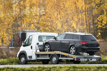 car breakdown and towing on a country road. A tow truck is transporting a damaged car that was...
