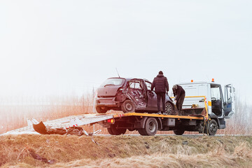 A tow truck loading a damaged black hatchback car on the highway after a collision. The car was hit...