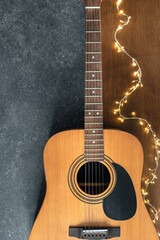 Acoustic guitar and garland on a textured black and wooden background, top view.