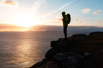 Silhouetted hiker with backpack admiring the sunset by the sea
