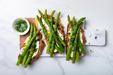 Grilled toasts with sourdough bread with green asparagus, ricotta, lemon zest and herb oil on...