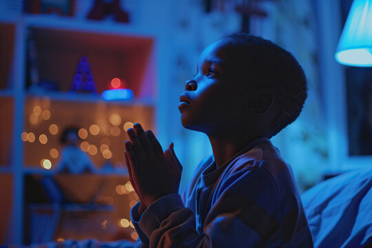 African American boy prays to god in dark children room. Cinematic effect