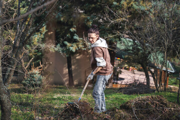 A young woman removes dry grass and cleans the soil in the spring garden of a country house. Spring work in the garden, preparing land for planting - 746381604