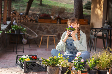 Young adult happy European woman on the terrace of a country house with a pot of spring flowers in her hands. Gardening as a hobby and spring lifestyle - 746385037