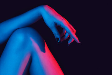 woman's manicured hand lies on her knee with a neon light