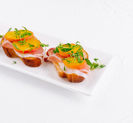 bruschetta with prosciutto and pear on white plate