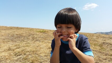 Happy kid sitting on the green field, on the Sunny day.. Boys Summer photo. Landscape mountain 