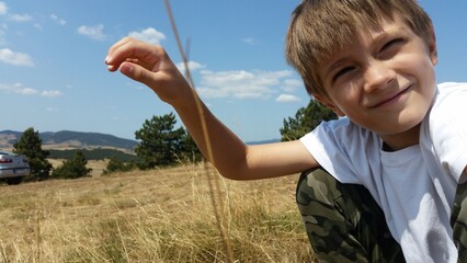 Happy kid sitting on the green field, on the Sunny day.. Boys Summer photo. Landscape mountain 
