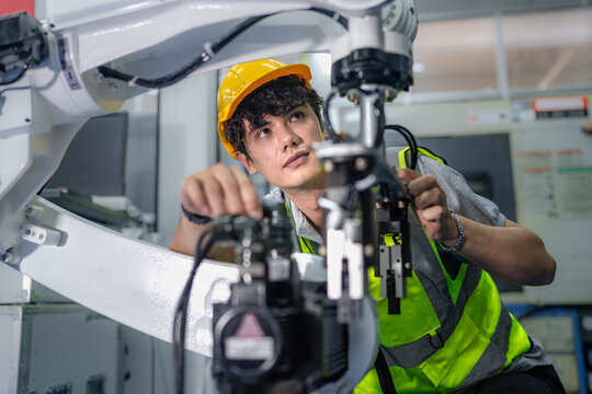 Robot maintenance engineer working on robot arm connection. Young adult man learning training robotic machine engineering in futuristic electronic education academy. Artificial intelligence technician