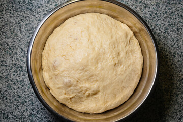 Raw dough for bread or buns made from white flour in an iron plate on the table, top view of baking...