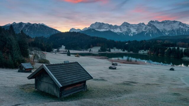 Time lapse of a gorgeous sunrise over the Alps at the scenic Gerold lake (Geroldsee) in Bavaria, Germany. With iconic cabin in the foreground on frozen meadow
