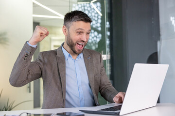 Ecstatic businessman celebrating success with fist pump at workplace