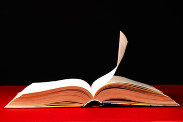 Pages of a thick book are turned on a red and black background, space for text.