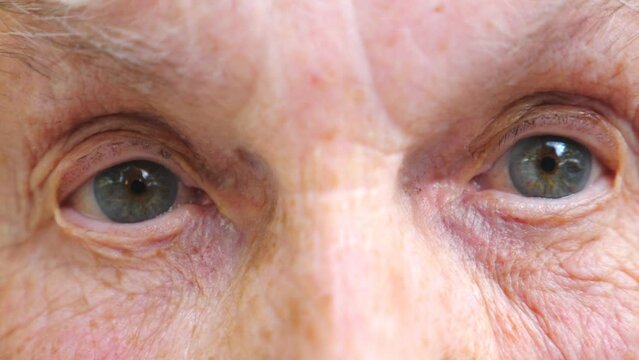 Elderly woman watching into camera and strongly screwing up her eyes. Close up of wrinkled female face with wide eyes showing surprise emotions. Granny with amazed facial expression. Slow motion