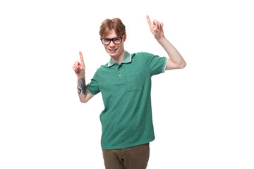 a young man with red hair in a green T-shirt gesticulates joyfully with his hands pointing to the...