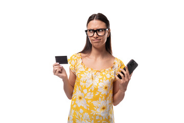 young brunette woman with straight hair dressed in a casual yellow T-shirt looks at the bank card data in her hands to use banking on her phone