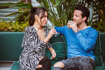 Multiethnic smiling couple sits on couch, having conversation in the terrace of a modern bar with...