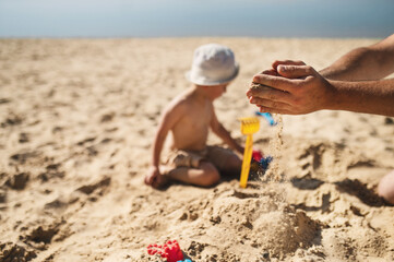 dad and son are building a sand castle on the beach. Hands and sand slipping through fingers close-up. Games on the beach on a hot summer day