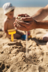 dad and son are building a sand castle on the beach. Hands and sand slipping through fingers close-up. Games on the beach on a hot summer day