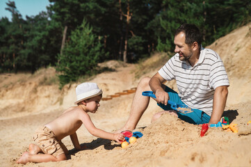 Father and 3 years son on beach building sand castle with plastic toys . single father solo parent. Involved parenting. Relaxing and playing outdoors with family