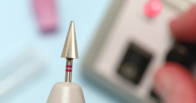 A specialist checks the balancing of a new carbide cutter for hardware manicure with a red notch, increases and decreases the rotation speed of the cutter