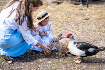 Mom and small daughter feeding rabbits and birds on farm