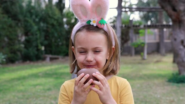 Easter egg hunt. Excited emotion surprise adorable child girl with dirty mustache mouth in bunny ears rabbit costume hold and eat Easter chocolate egg. Children positive emotions. Kid happy Easter