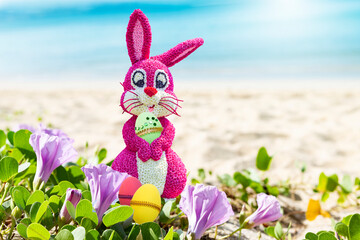 Pink Easter bunny holding green egg on tropical beach, Happy Easter card background idea