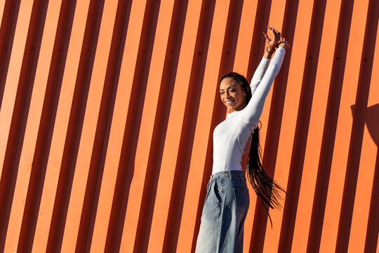 Smiling woman standing with arms raised in front of wall