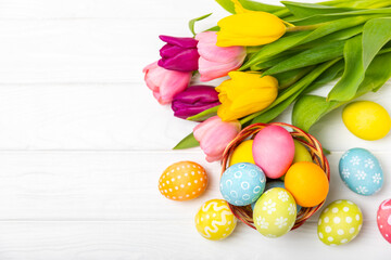Naklejka na ściany i meble Easter basket filled with colorful eggs and a bouquet of tulips on a textured wooden table. Easter celebration concept. Colorful easter handmade decorated Easter eggs. Place for text. Copy space