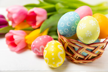 Fototapeta na wymiar Easter basket filled with colorful eggs and a bouquet of tulips on a textured wooden table. Easter celebration concept. Colorful easter handmade decorated Easter eggs. Place for text. Copy space