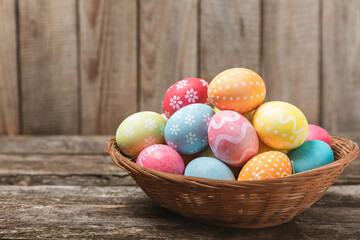Easter basket filled with colorful eggs and a bouquet of tulips on a textured wooden table. Easter celebration concept. Colorful easter handmade decorated Easter eggs. Place for text. Copy space