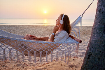 Young blissful calm woman wearing wireless headphones lie in a hammock and enjoy relaxing music