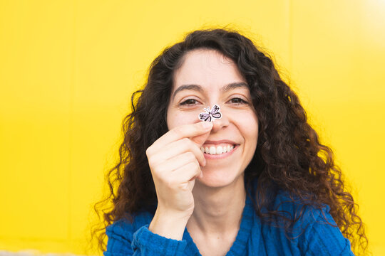 Happy woman holding butterfly sticker on nose against yellow background
