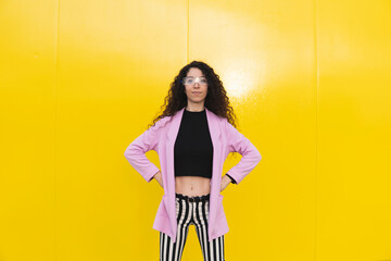 Confident woman standing with arms akimbo against yellow background
