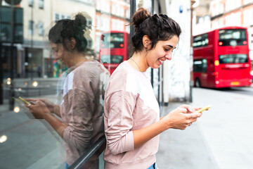 Happy woman in London smiling and using her smartphone