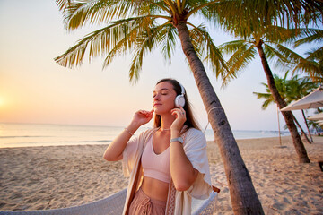 Young blissful happy carefree joyful calm woman wearing white wireless headphones with closed eyes enjoy relaxing music by the sea