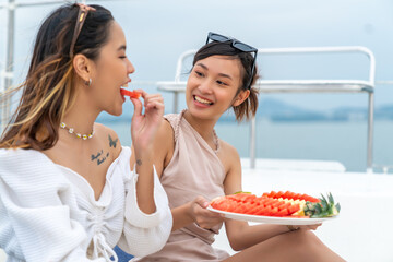 Happy Asian woman friends enjoy outdoor lifestyle eating fresh fruit together during travel nature...
