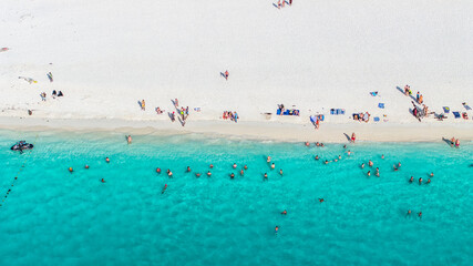 aerial top view of a white sand beach with crystal clear turquoise water and people on the beach...