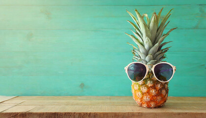 Ripe pineapple in stylish sunglasses over wooden table background. Tropical summer vacation concept. top view - obrazy, fototapety, plakaty