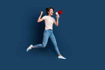 Full size photo of attractive young woman jump hold toa fist celebrate wear trendy white clothes isolated on dark blue color background