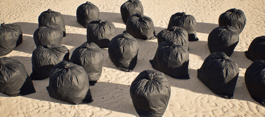 A large amount of black trash bags left on tropical beach with rippled sand.