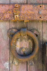 Rusty knocker and bolt on an old wooden door. Old paint and wood texture are visible.