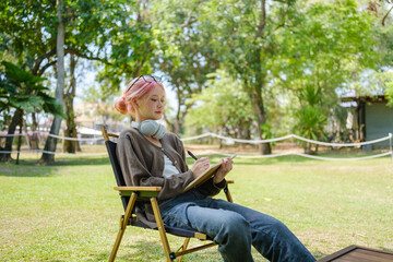 Woman among nature wearing glasses and head phone reading a book.