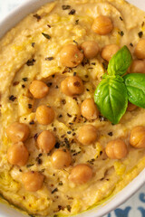 A bowl of hummus with chickpeas and basil on a table