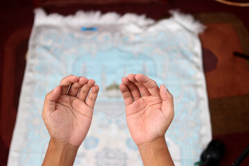 On a prayer mat at home, an Indonesian man raises open palms in dua to Allah, seeking forgiveness...