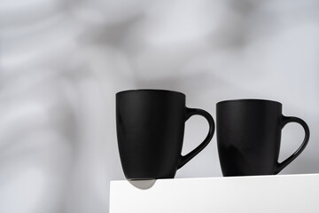 Two black ceramic mugs on gray background with shadows